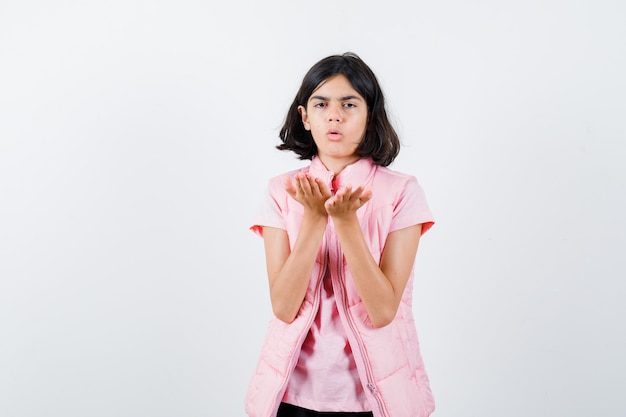 Portrait of a little girl in white t-shirt and puffer vest sending kiss with hands