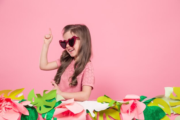 Portrait of a little girl with sunglasses on a pink wall