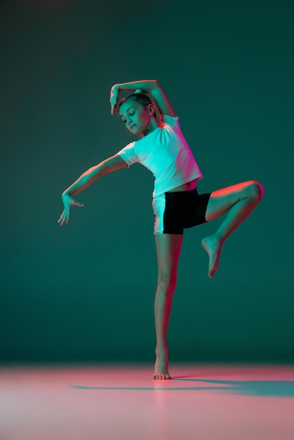 Portrait of little sportive girl rhytmic gymnast training isolated over green background in neon