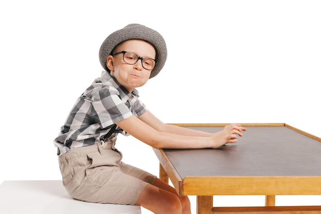 Портрет маленького стильного мальчика, сидящего, позирующего изолированно на белом студийном фоне