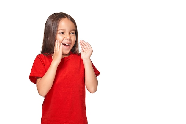 赤いTシャツで怖がって興奮している小さな驚きの女の子の肖像画。白い背景に分離