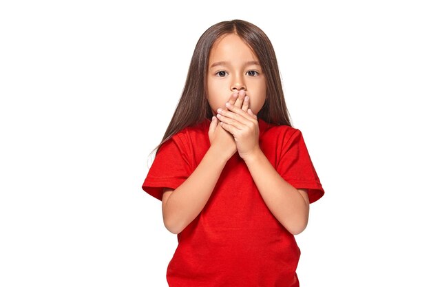 赤いTシャツで怖がって興奮している小さな驚きの女の子の肖像画。白い背景に分離