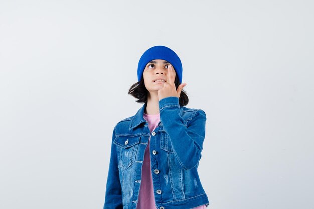 Portrait of little woman pointing up in denim jacket and beanie looking positive