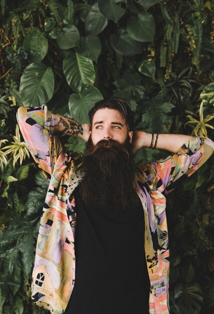 Portrait of long bearded young man standing in front of green leaves