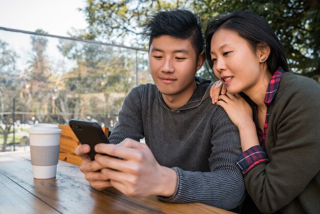 Portrait of lovely asian couple looking at the mobile phone while sitting and spending time at the coffee shop. 