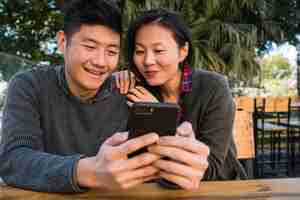 Free photo portrait of lovely asian couple looking at the mobile phone while sitting and spending time at the coffee shop.