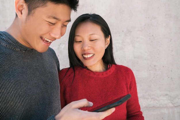 Free photo portrait of lovely asian couple looking at the mobile phone while spending good time together.