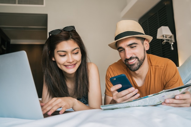 Portrait of lovely couple organizing their trip with laptop and mobile phone at the hotel room