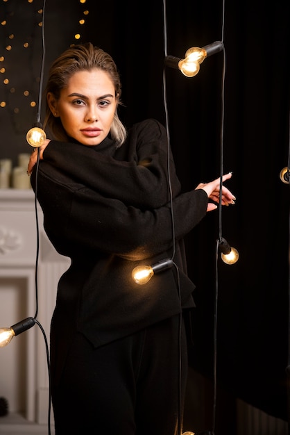 Портрет прекрасной женщины, позирующей в темном свитере, стоящем возле ламп.