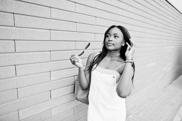 Ritratto di una bella giovane donna afroamericana in posa con occhiali da sole contro un muro di mattoni sullo sfondo foto in bianco e nero