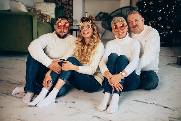 Portrait of loving cheerful family in sweaters and jeans wearing funny festive Christmas glasses.