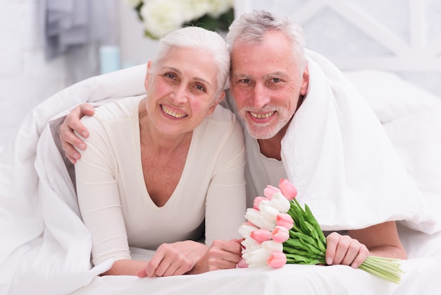Portrait of loving elder couple lying on bed with beautiful flower bouquet