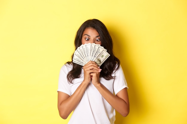 Portrait of lucky africanamerican girl winning money prize holding cash and looking amazed standing