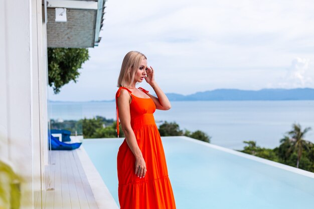 Portrait of luxury looking woman in red orange evening dress in rich hotel