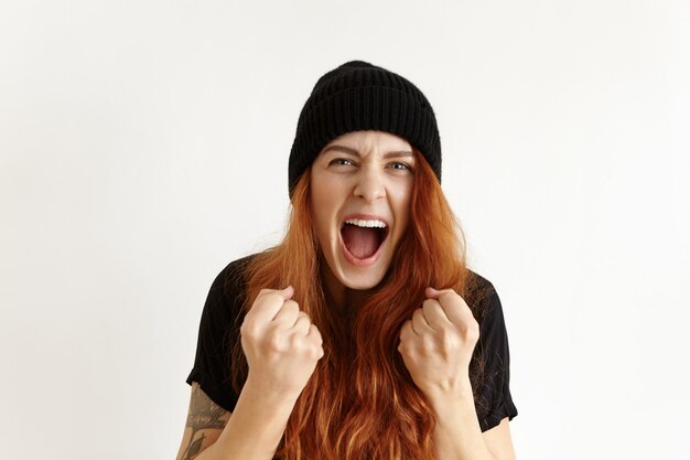 Portrait of mad and furious young redhead woman in hipster hat expressing rage and anger