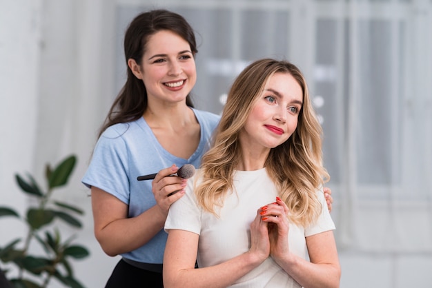 Portrait of makeup artist using brush and happy blond woman