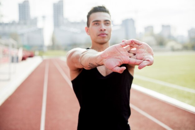 Portrait of a male athlete stretching her hands before running on race track