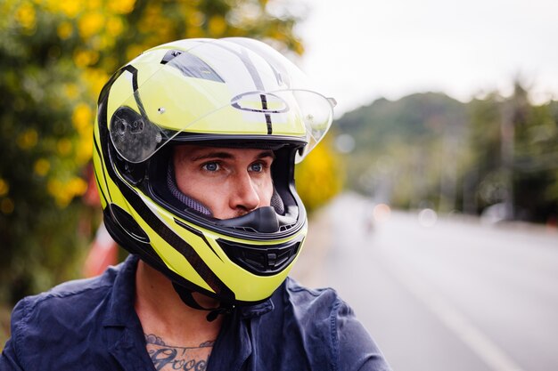 Portrait of male biker in yellow helmet on motorbike on side of busy road in Thailand