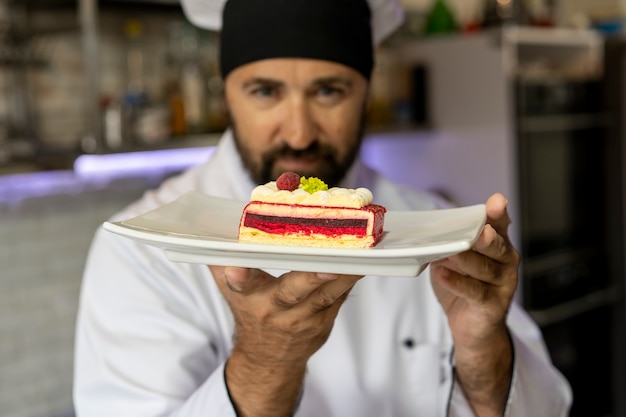 Портрет шеф-повара-мужчины на кухне с тарелкой десерта