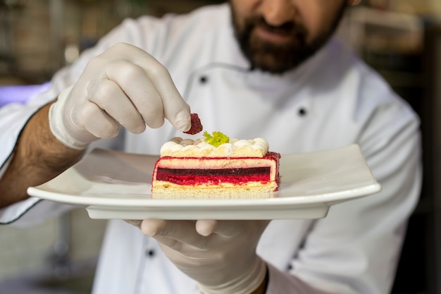 Portrait of male chef in the kitchen holding plate of dessert