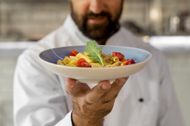 Portrait of male chef in the kitchen holding plate of food