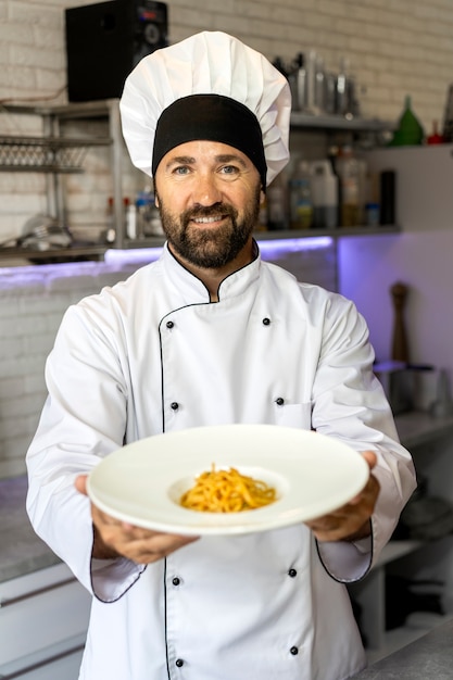Portrait of male chef in the kitchen holding plate of food