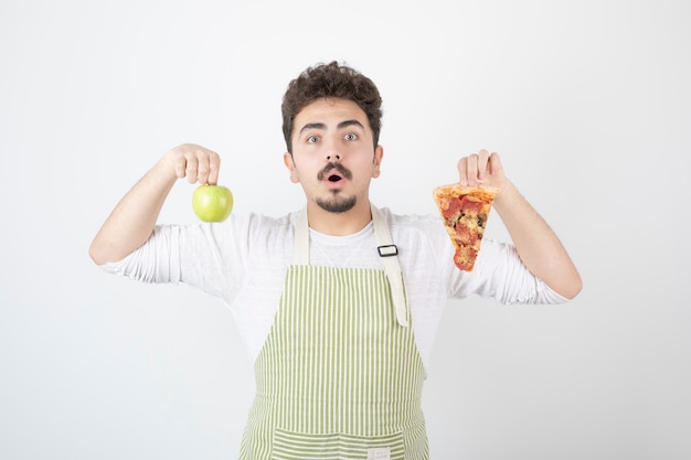 Portrait of male cook holding pizza and green apple on white 