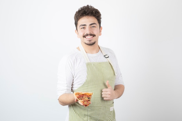 Portrait of male cook holding slice of pizza and giving thumbs up