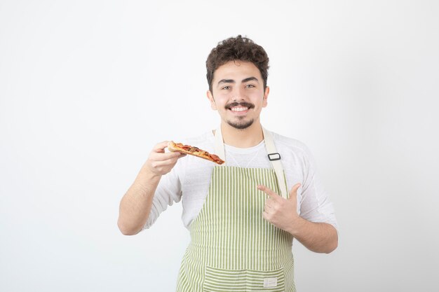 Portrait of male cook holding slice of pizza and pointing at it