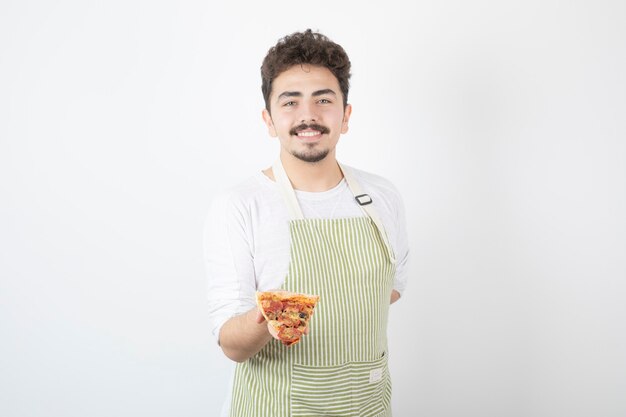 Portrait of male cook holding slice of pizza on white 