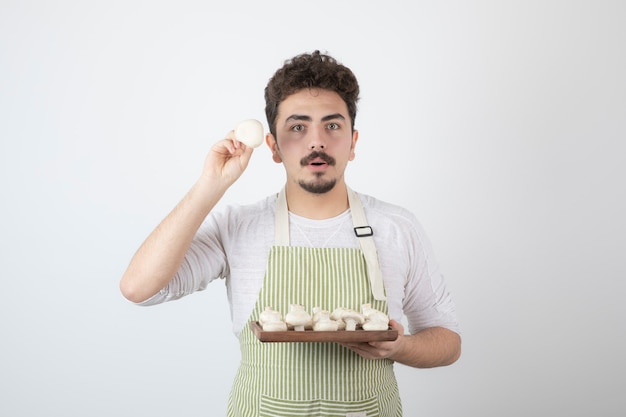 Portrait of male cook showing raw mushrooms on white 