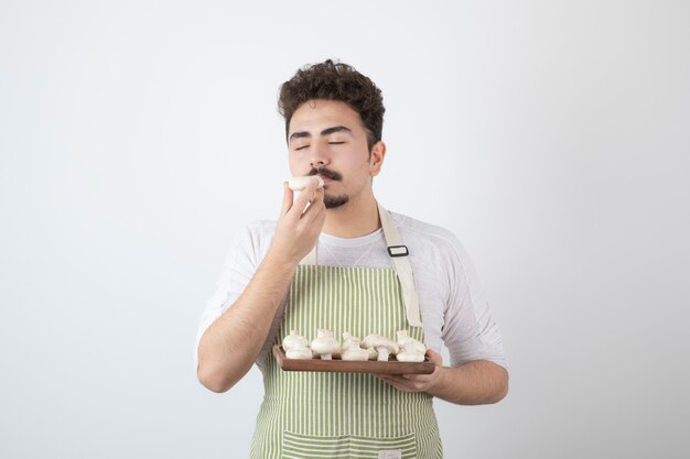 Portrait of male cook smells raw mushrooms on white 