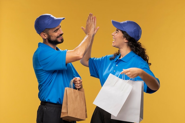 Портрет мужчин и женщин-доставщиков, дающих друг другу пять, держа в руках бумажные пакеты