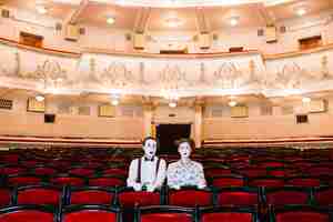 Free photo portrait of male and female mime artist sitting on red chair in the auditorium