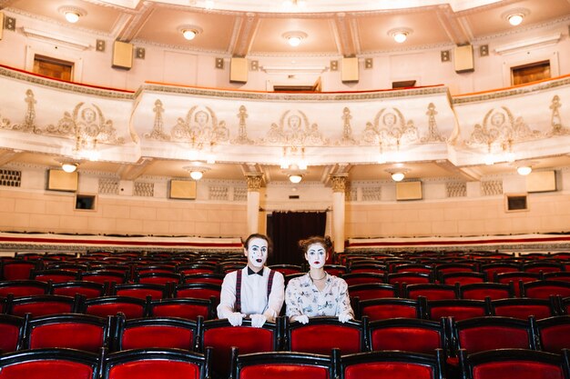 Portrait of male and female mime artist sitting on red chair in the auditorium