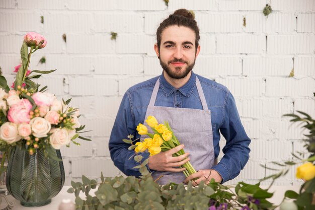 白い壁に黄色のチューリップを手で押し、男性の花屋の肖像画