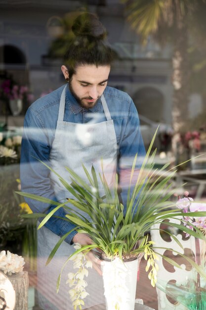 Portrait of a male florist placing the vase seen through glass