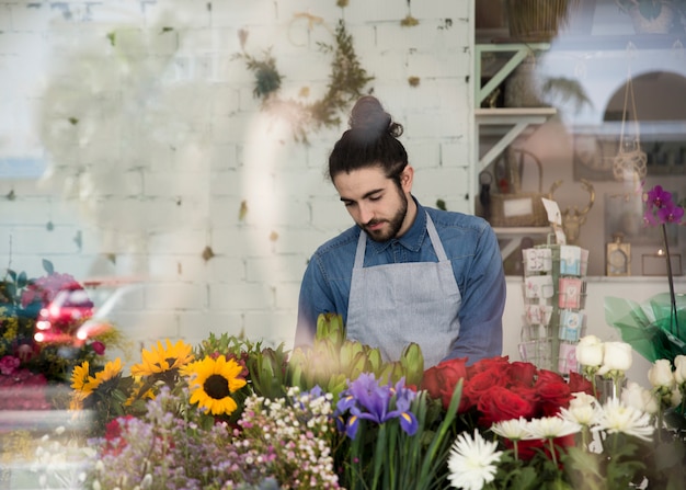 Foto gratuita ritratto di un fiorista maschio che sta dietro i fiori variopinti nel negozio di fiore