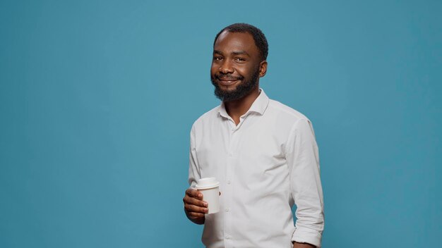 Portrait of male freelancer enjoying cup of coffee in studio, holding mug with latte beverage on work break and timeout. Executive manager smiling and drinking espresso at breakfast.