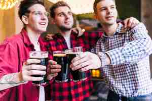 Foto gratuita ritratto dei vetri tintinnanti dell'amico maschio con birra in pub