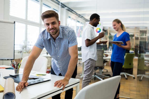 Free photo portrait of male graphic designer smiling while coworkers interacting in background