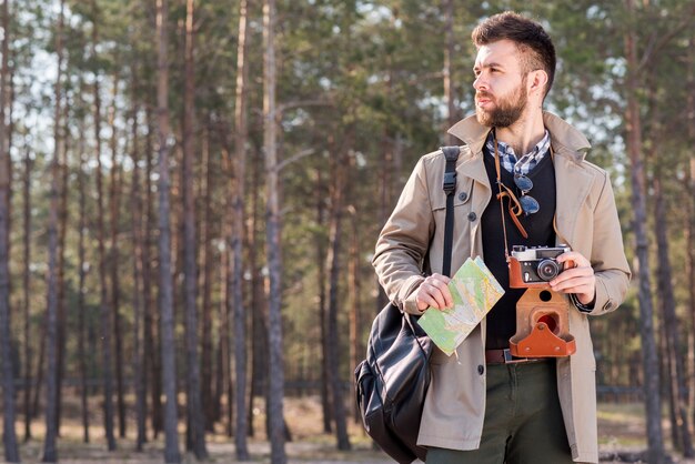 Portrait of a male hiker with camera and map standing in the forest