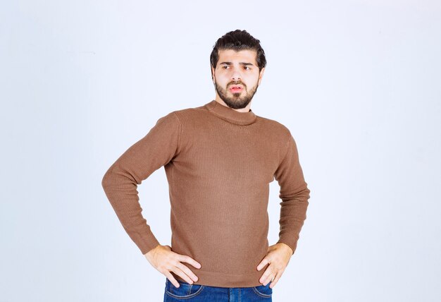 Портрет мужской модели в коричневом свитере, стоящем над белой стеной.