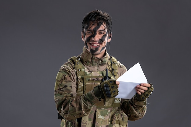 Portrait of male soldier in camouflage holding letter on dark wall