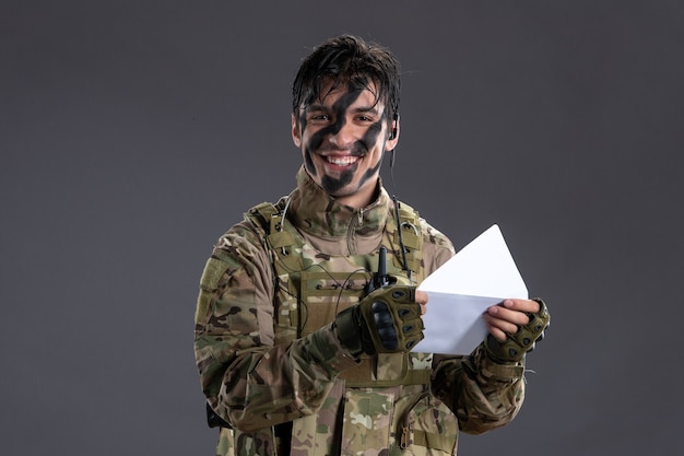 Портрет мужчины-солдата в камуфляже, держащего письмо на темной стене