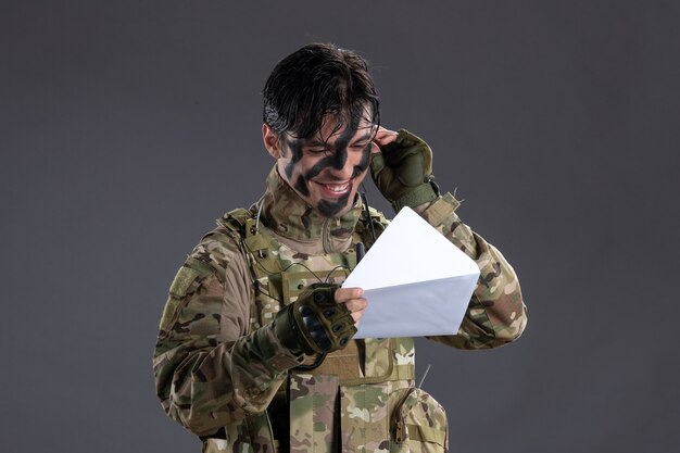 Portrait of male soldier in camouflage holding letter on the dark wall