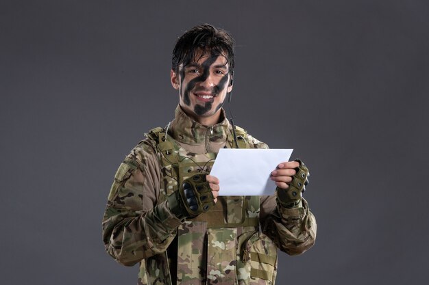 Portrait of male soldier in camouflage reading letter from family dark wall