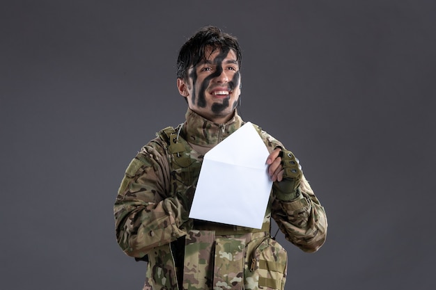 Portrait of male soldier in camouflage reading letter from family on a dark wall