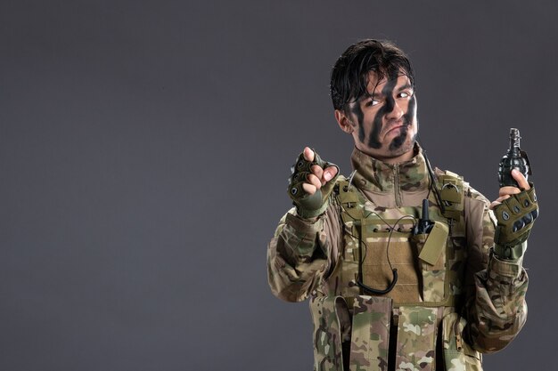 Portrait of male soldier in camouflage with grenade on dark wall