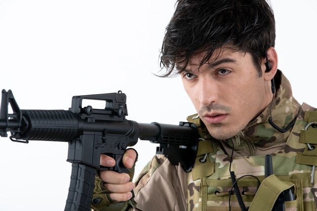 Portrait of male soldier in military uniform with machine gun white wall